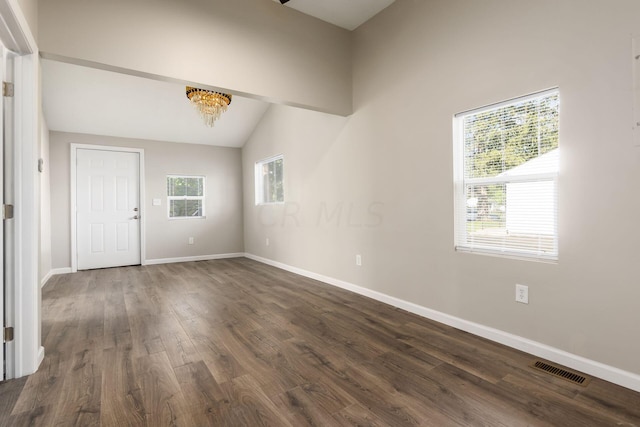 spare room featuring dark hardwood / wood-style flooring, lofted ceiling, and an inviting chandelier