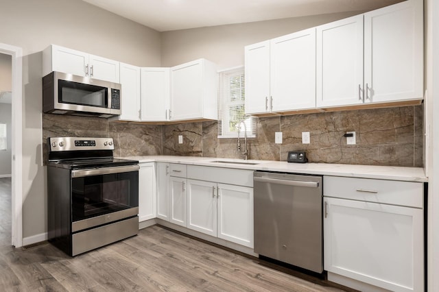 kitchen with sink, white cabinetry, stainless steel appliances, and light hardwood / wood-style flooring