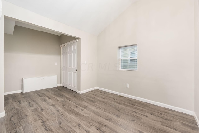 empty room with high vaulted ceiling and wood-type flooring