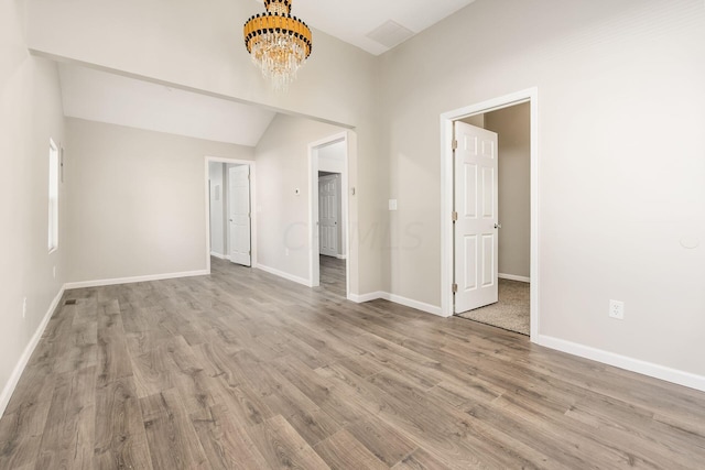 unfurnished room with light hardwood / wood-style flooring, a chandelier, and vaulted ceiling