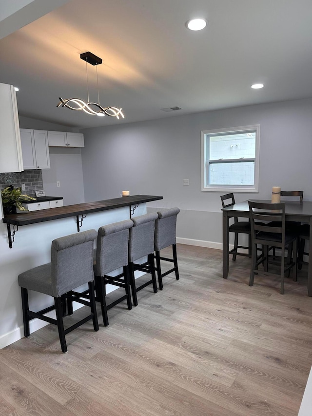 kitchen featuring white cabinetry, hanging light fixtures, light hardwood / wood-style flooring, backsplash, and a breakfast bar area