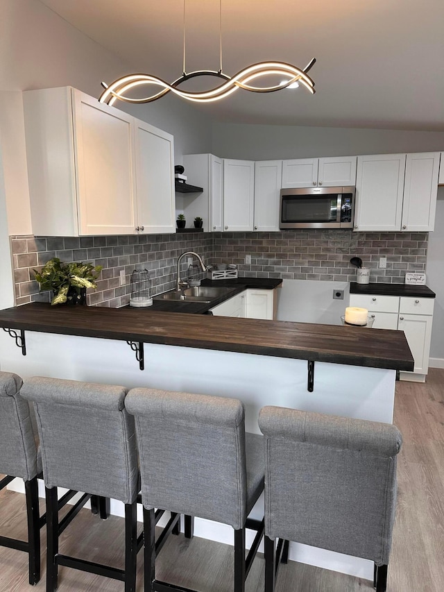 kitchen with pendant lighting, light wood-type flooring, tasteful backsplash, a kitchen bar, and white cabinetry