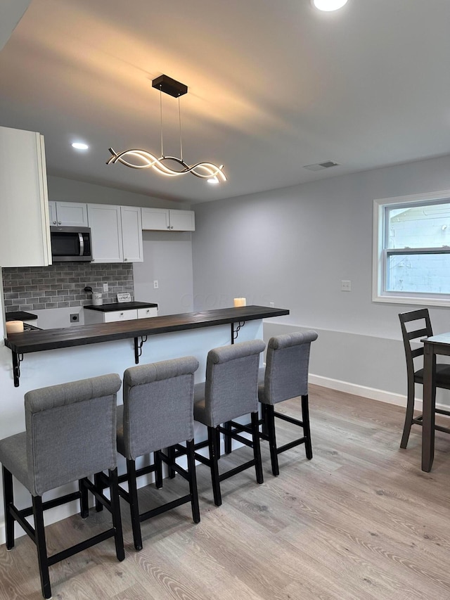 kitchen with white cabinets, light wood-type flooring, tasteful backsplash, decorative light fixtures, and a breakfast bar area