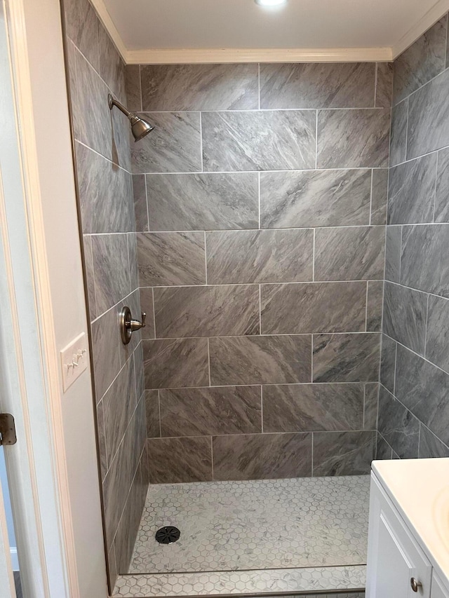 bathroom with vanity, ornamental molding, and tiled shower