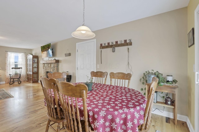 dining area with light wood-type flooring and a stone fireplace