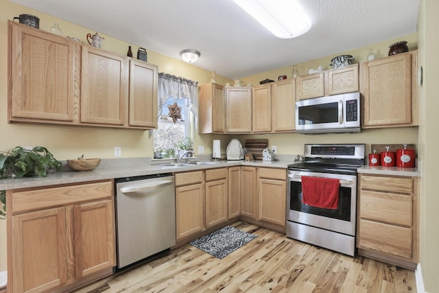 kitchen with stainless steel appliances, sink, a textured ceiling, light hardwood / wood-style floors, and light brown cabinetry