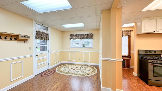 kitchen with a drop ceiling, wood-type flooring, ornate columns, white cabinetry, and stainless steel range with gas stovetop