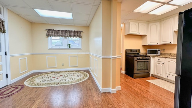 kitchen featuring a drop ceiling, white cabinets, black appliances, and light wood-type flooring