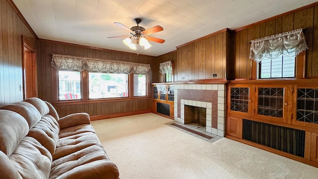 living room featuring a tiled fireplace, wood walls, light colored carpet, and a healthy amount of sunlight