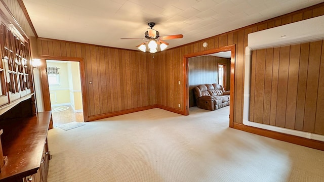 unfurnished room with light carpet, crown molding, ceiling fan, and wood walls