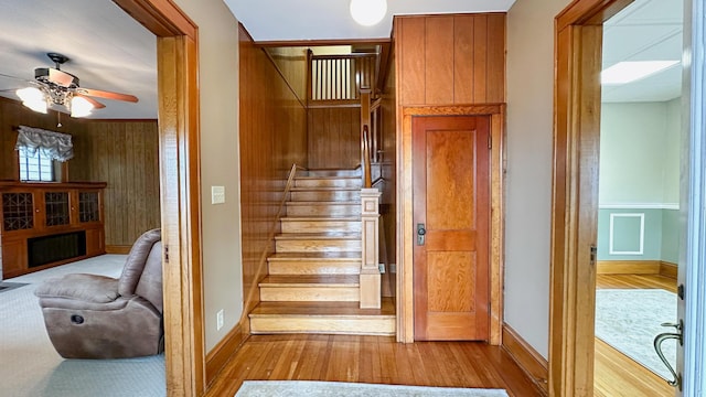 staircase with wood-type flooring, ceiling fan, and wood walls