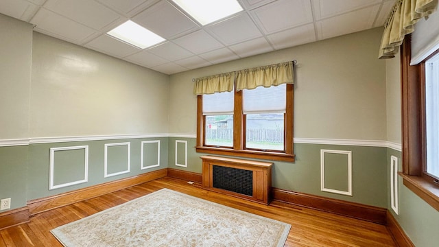 unfurnished room with radiator heating unit, light wood-type flooring, and a drop ceiling