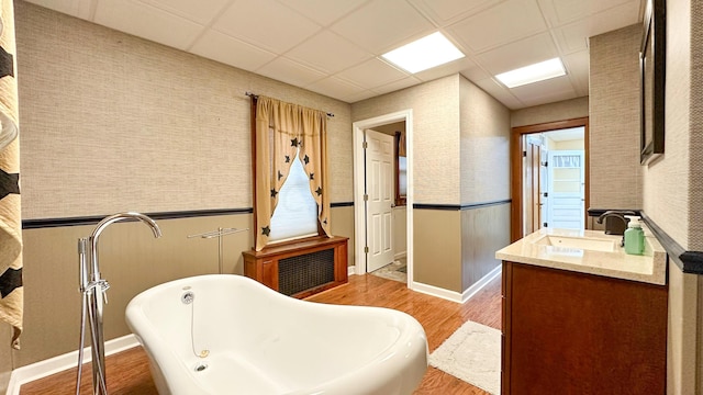 bathroom with vanity, hardwood / wood-style floors, a drop ceiling, and a bathtub