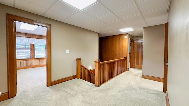 hallway with a paneled ceiling, light colored carpet, and wooden walls