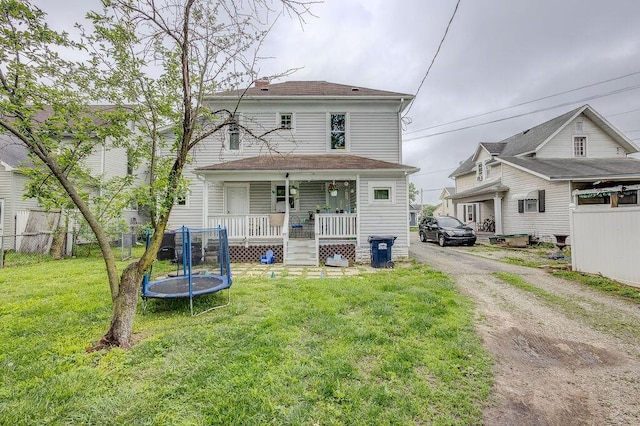 back of property featuring covered porch, a trampoline, and a yard