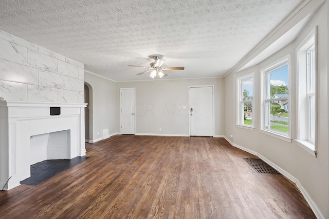 unfurnished living room with a tile fireplace, ceiling fan, dark wood-type flooring, crown molding, and a textured ceiling