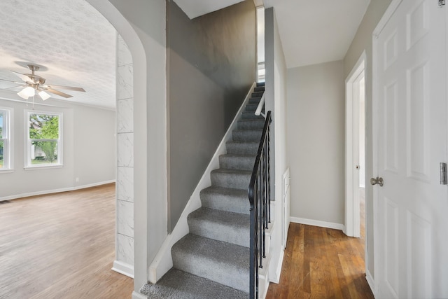 stairway featuring ceiling fan, wood-type flooring, and a textured ceiling