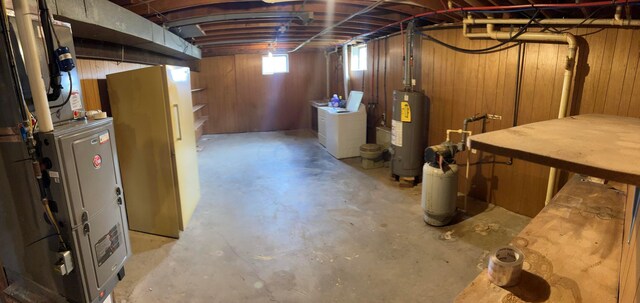 basement featuring gas water heater, washer and clothes dryer, and wood walls