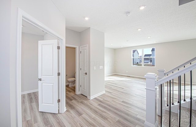 hall with a textured ceiling, light wood-style flooring, baseboards, stairway, and recessed lighting