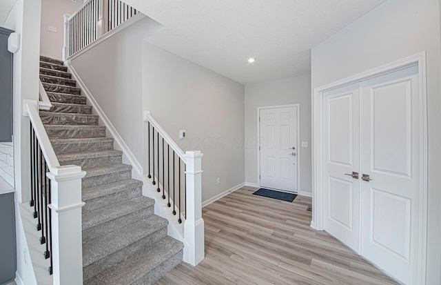 foyer entrance featuring stairway, light wood finished floors, a textured ceiling, baseboards, and recessed lighting