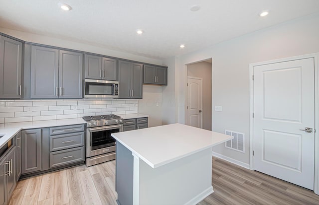 kitchen featuring gray cabinetry, light wood-style flooring, stainless steel appliances, visible vents, and decorative backsplash