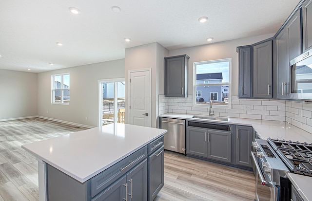 kitchen with gray cabinets, a sink, appliances with stainless steel finishes, and light wood finished floors