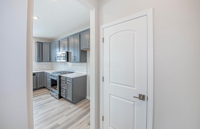 kitchen with light countertops, light wood-type flooring, stainless steel appliances, gray cabinetry, and decorative backsplash