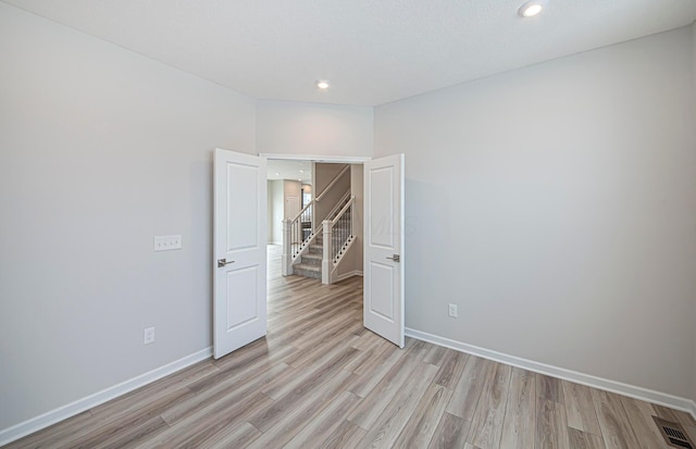 unfurnished room featuring visible vents, baseboards, recessed lighting, stairway, and light wood-type flooring