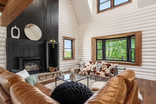 living room featuring rustic walls, wood-type flooring, beam ceiling, high vaulted ceiling, and a fireplace