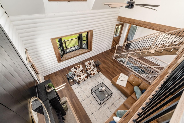 living room featuring ceiling fan, wood walls, wood-type flooring, and a high ceiling