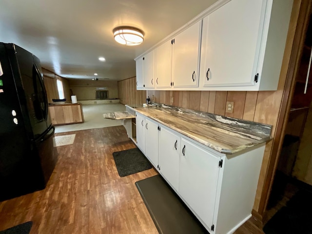 kitchen with hardwood / wood-style flooring, black fridge, and white cabinetry