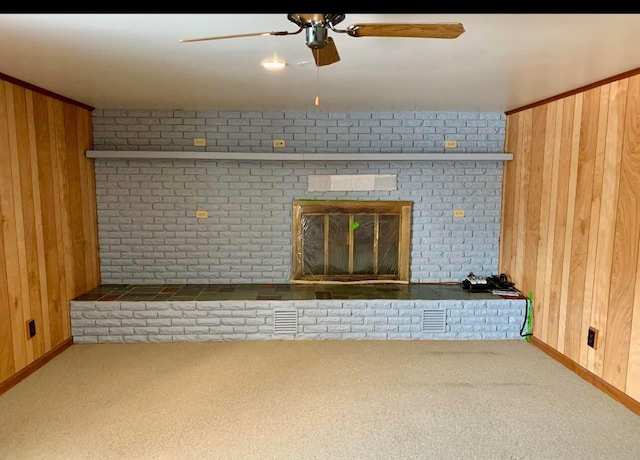 unfurnished living room with carpet floors, a brick fireplace, ceiling fan, and wood walls