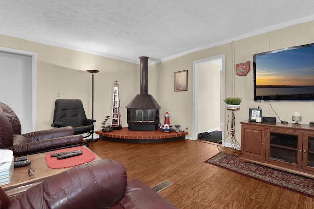 living room featuring a textured ceiling, hardwood / wood-style flooring, a wood stove, and ornamental molding