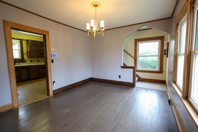 spare room with an inviting chandelier, dark wood-type flooring, and crown molding