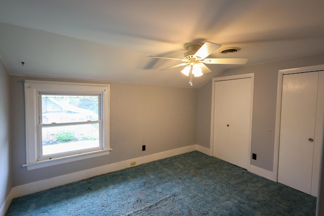 unfurnished bedroom with dark colored carpet, two closets, ceiling fan, and lofted ceiling