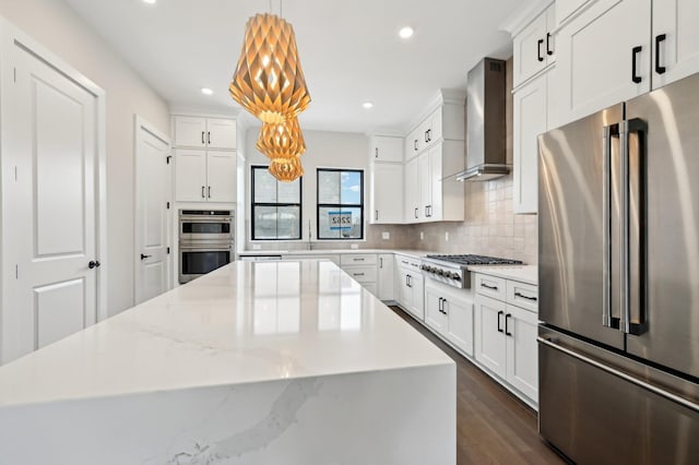 kitchen featuring appliances with stainless steel finishes, pendant lighting, white cabinets, a center island, and wall chimney range hood