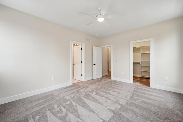 unfurnished bedroom with light carpet, a walk in closet, a closet, and ceiling fan