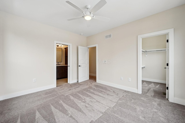 unfurnished bedroom featuring ensuite bath, a spacious closet, light colored carpet, a closet, and ceiling fan