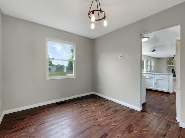 unfurnished dining area featuring dark hardwood / wood-style flooring, a healthy amount of sunlight, and an inviting chandelier