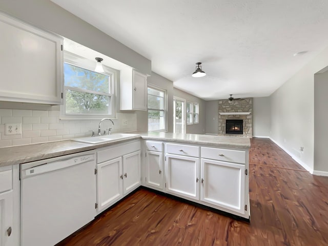 kitchen with white dishwasher, dark hardwood / wood-style floors, a stone fireplace, and white cabinets