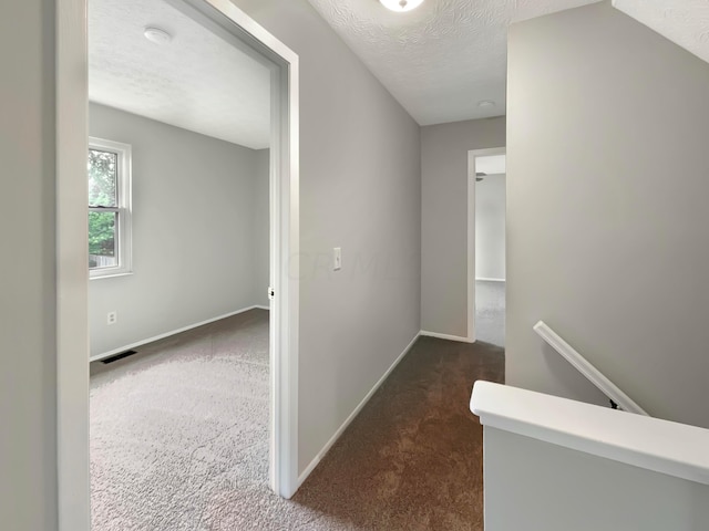 corridor featuring dark colored carpet and a textured ceiling