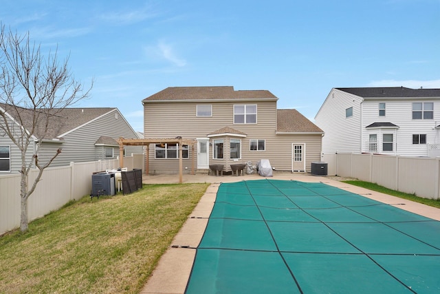 rear view of house with a yard, a covered pool, a patio area, and central air condition unit