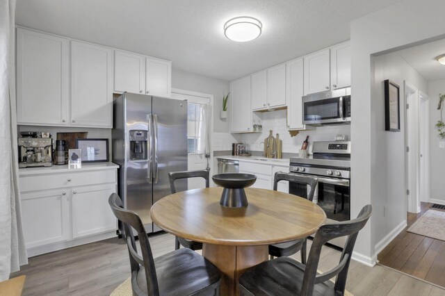 kitchen featuring appliances with stainless steel finishes, light wood-type flooring, white cabinetry, and backsplash