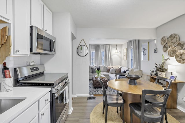 kitchen with appliances with stainless steel finishes, tasteful backsplash, a textured ceiling, dark wood-type flooring, and white cabinets