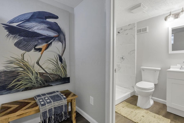 bathroom featuring vanity, a textured ceiling, tiled shower, wood-type flooring, and toilet