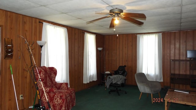 sitting room with wood walls, ceiling fan, and dark carpet