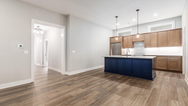 kitchen featuring pendant lighting, stainless steel refrigerator, hardwood / wood-style floors, tasteful backsplash, and an island with sink