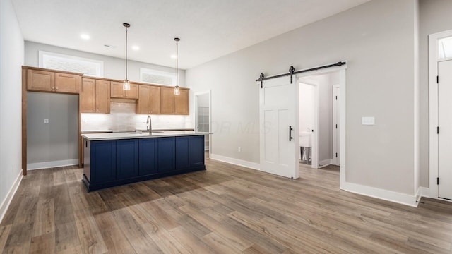 kitchen with pendant lighting, sink, a kitchen island with sink, a barn door, and dark wood-type flooring