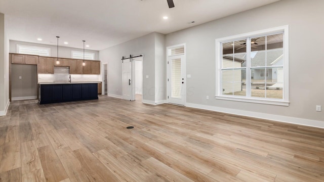 unfurnished living room featuring a barn door, sink, ceiling fan, and light hardwood / wood-style floors