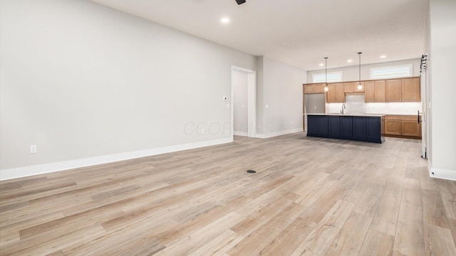 unfurnished living room featuring ceiling fan, sink, and light wood-type flooring